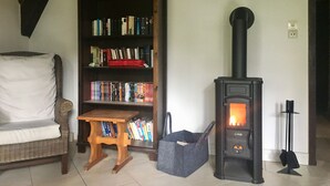 Un salon comprenant une bibliothèque, un canapé, une petite table en bois, un poêle en bois noir et un sac gris.