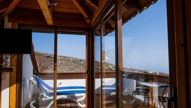 A wooden deck with a table and chairs, overlooking a hilly landscape.