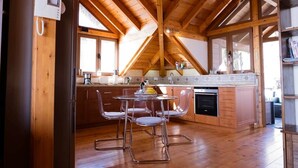 A wooden interior with a kitchen area featuring a dining table with chairs, a refrigerator, and a stove.