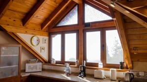 A kitchen with wooden beams, a large window, a clock, and various appliances.