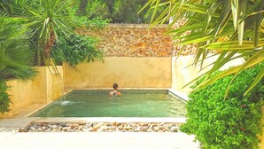 A person in a small, rectangular pool with clear water, surrounded by lush greenery and a stone wall. - Villagehouse, AC, pool, unoverlooked patio, stores restaurants walking distance (Saint-Nazaire-D'aude)