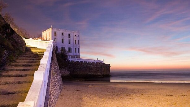A white building with a stone wall and steps leading down to a beach.