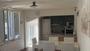 A modern living room with a white sofa, a dining table, and a kitchen area with a microwave and refrigerator.