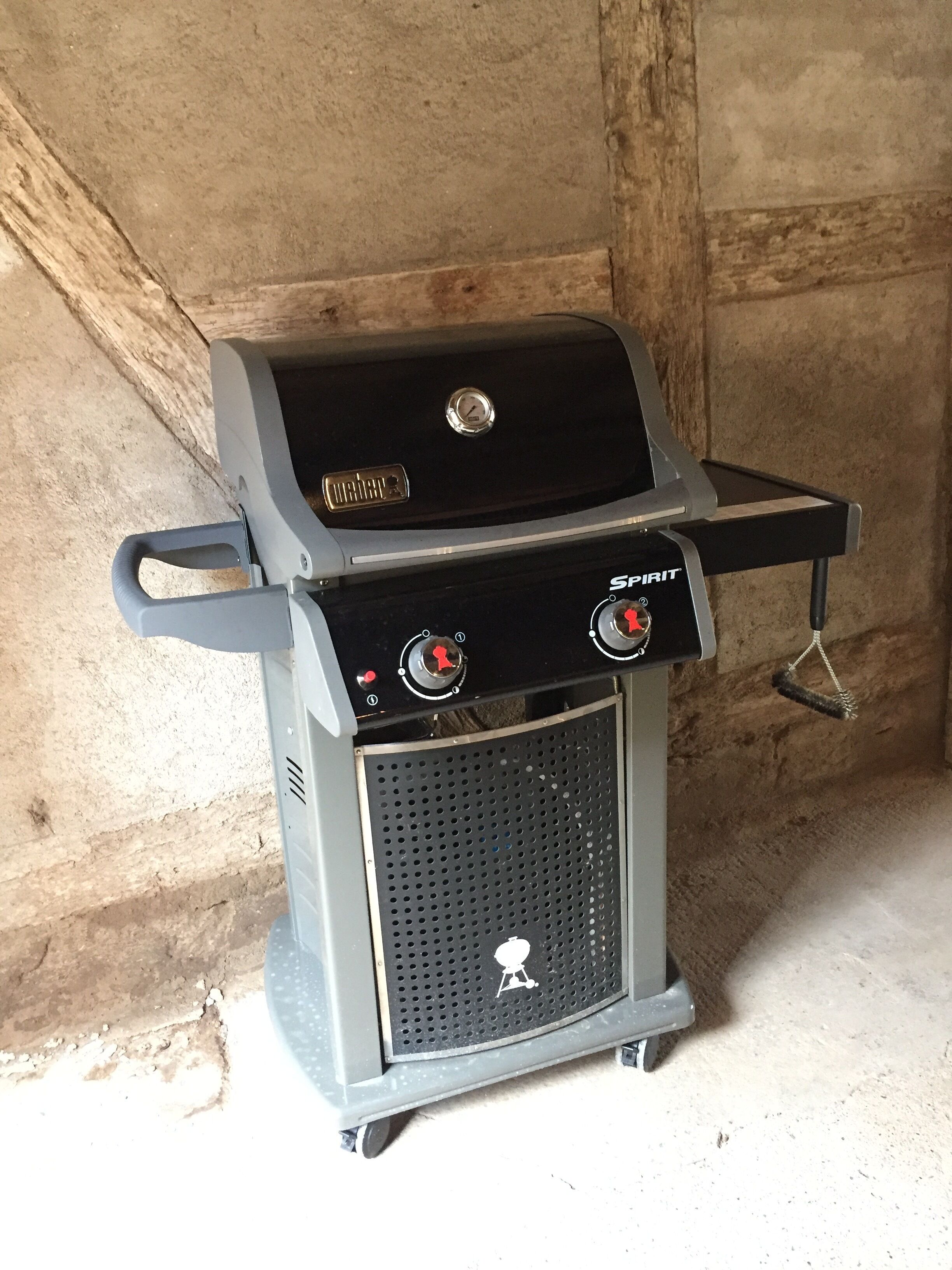 A portable gas grill with digital controls and a side burner, set against a concrete wall.