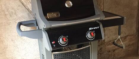 A portable gas grill with digital controls and a side burner, set against a concrete wall.