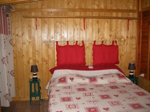 Ein Zimmer mit Holzwänden, einem Bett, zwei Nachttischen und einem roten Kopfteil.