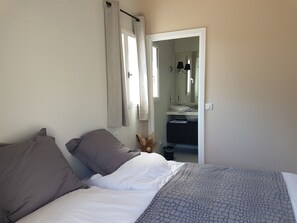Een slaapkamer met een bed, kussens, een nachtkastje, een spiegel en een badkamer zichtbaar door een open deur.
