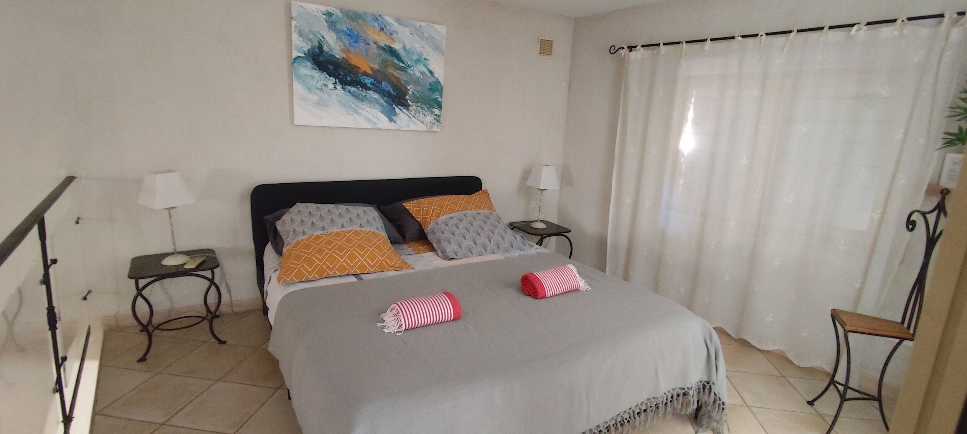 Un dormitorio con una cama, dos mesitas de noche, una lámpara, un cuadro y una cortina.