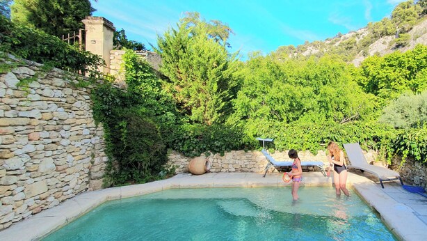 A swimming pool with stone walls, surrounded by greenery and a clear sky.