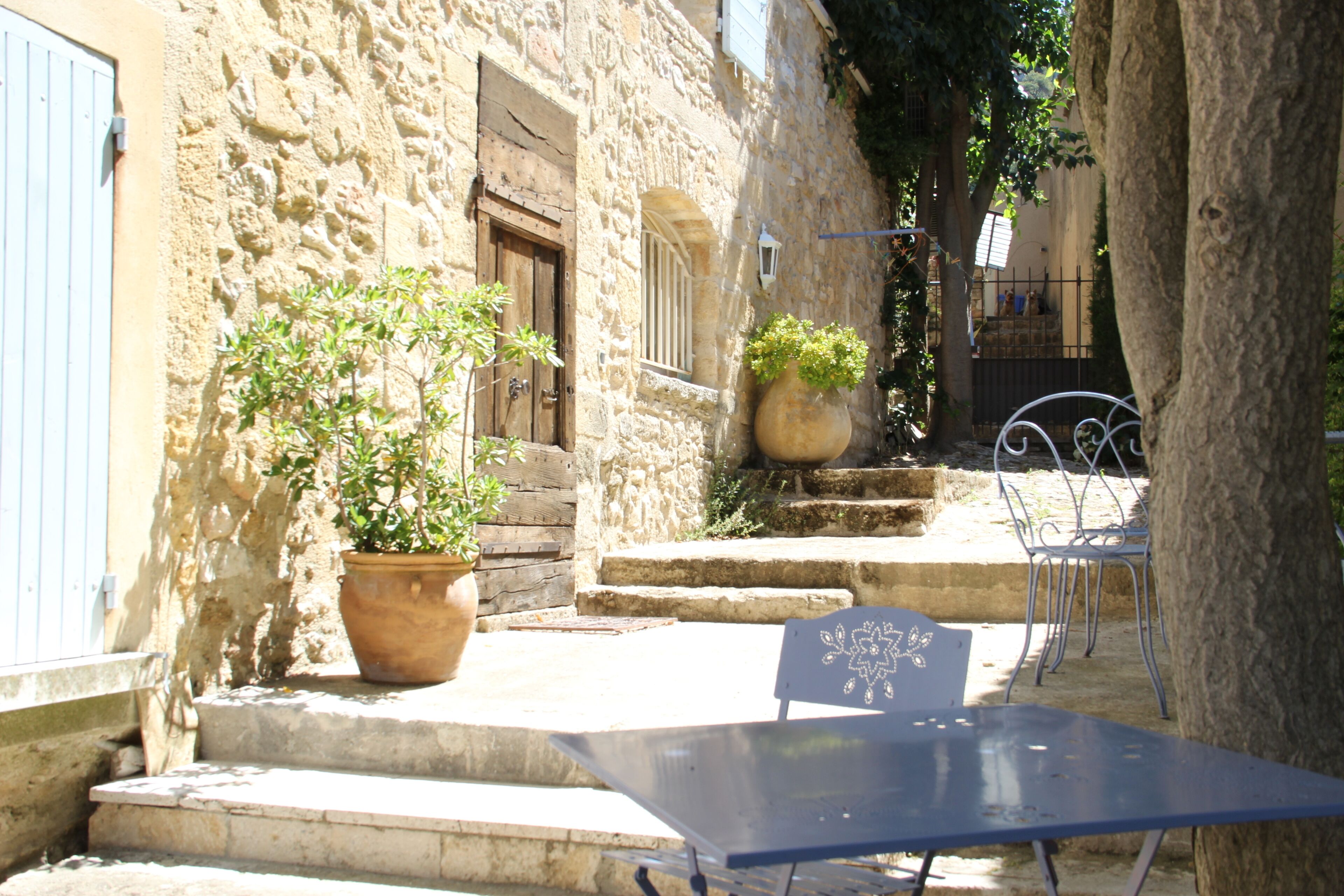 A narrow stone alley with steps leading to a door, a potted plant, and a metal table with chairs.