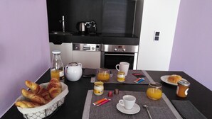 A breakfast setup with croissants, juice, coffee, and pastries on a table with a kitchen in the background. - Appart Aix Mazarin 3 stars-T2 with air conditioning in the historic city centre (Aix-en-Provence)