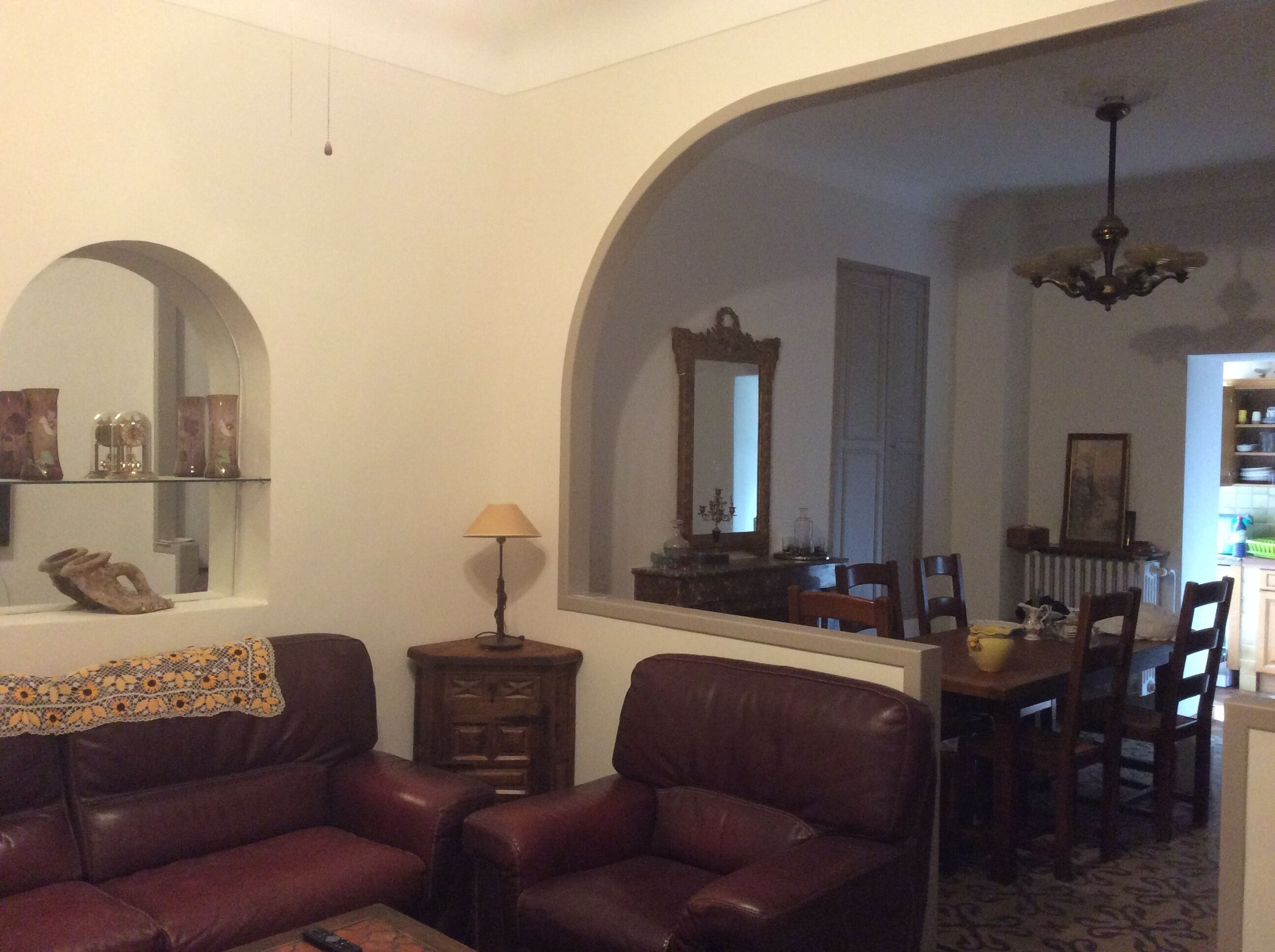 Una sala de estar con sofá, lámpara, espejo y un comedor con sillas y mesa.