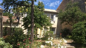 Um pátio com um edifício, telhado telhado e um jardim com diversas plantas e flores.