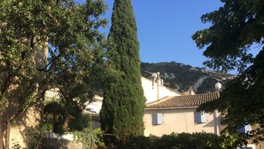 Um edifício tradicional com telhado de azulejos, cercado por vegetação e um cenário montanhoso.