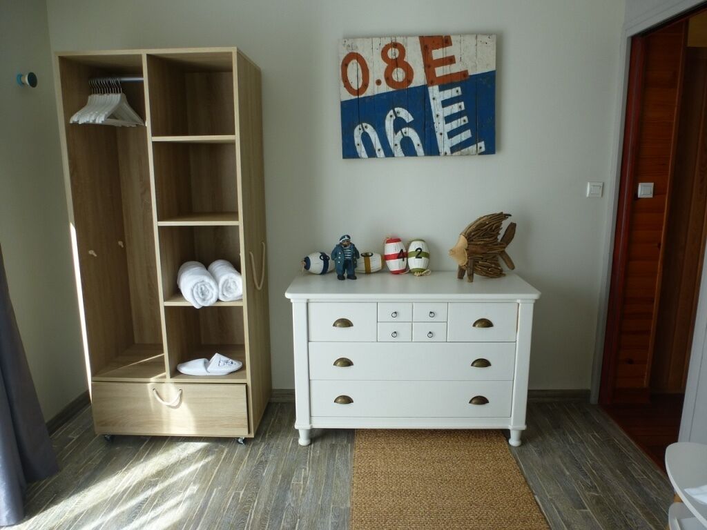 A room with a wooden wardrobe, a white dresser with drawers, a wall-mounted sign, and a small shelf with decorative items.