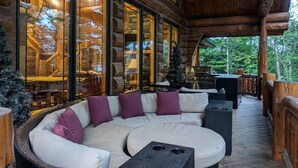 A log cabin with a large glass window, a white sofa with purple cushions, and a grill outside.