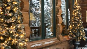 A log cabin with two Christmas trees in front of large windows.