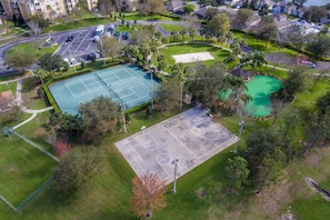 An aerial view of a sports complex with multiple tennis courts, surrounded by greenery and residential buildings.