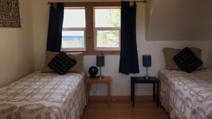 Une chambre avec deux lits, une fenêtre avec des rideaux, une petite table avec une lampe et un tableau accroché au mur.