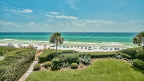 A beach view with a pathway leading to the beach, palm trees, and beach umbrellas.