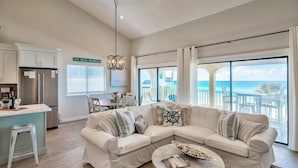 A modern living room with a beige sectional sofa, a small round table, and a view of the ocean through large windows.