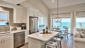 A modern kitchen with white cabinetry, a central island, and a dining area with a view of the ocean.