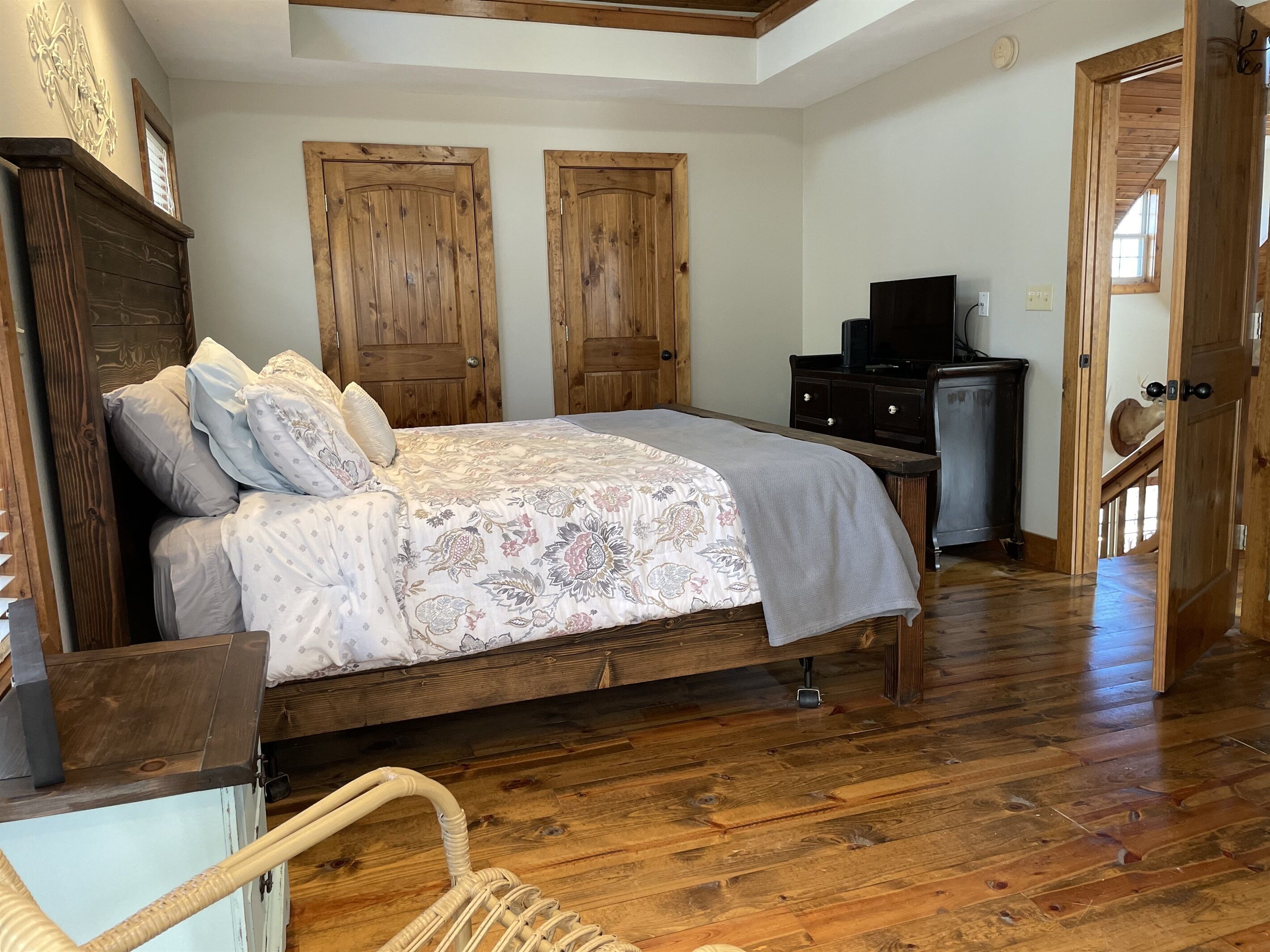 Une chambre à coucher avec un lit en bois, une commode, un téléviseur et une porte donnant sur une autre pièce.