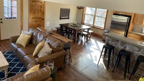 A spacious living room with a brown leather couch, a dining area with a wooden table, and a kitchen with a stainless steel refrigerator. - Sleeps 12, Pool, Marina, Quiet Side of Table Rock (Cassville)