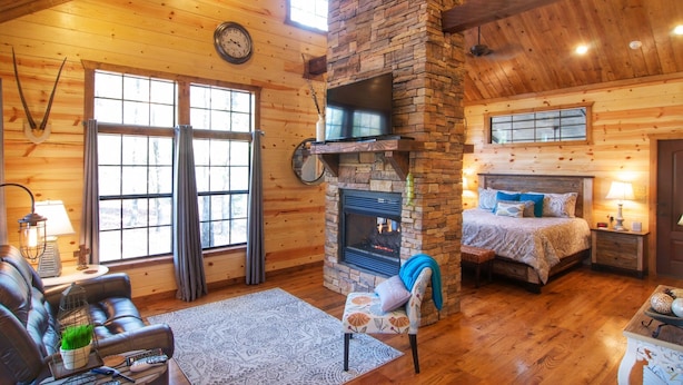 Ein gemütliches Blockhaus-Interieur mit Kamin aus Stein, einem Bett, einer Couch und einem an der Wand befestigten Fernseher.