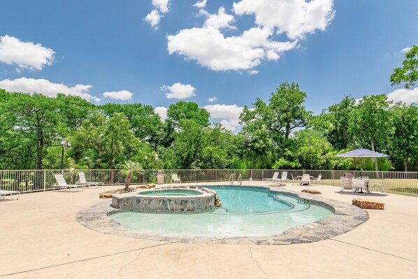 A swimming pool with a hot tub, surrounded by lounge chairs and a stone border.
