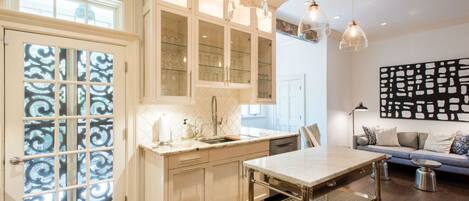 A modern kitchen with white cabinetry, a marble countertop, and pendant lighting.