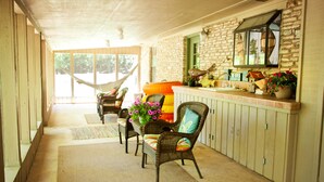 A covered porch with wicker furniture, a hammock, and a stone wall with a window.