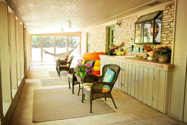 A covered porch with wicker furniture, a hammock, and a stone wall with a window.