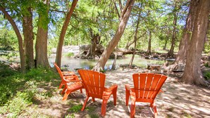 A campsite with orange chairs and a picnic table near a river, surrounded by trees.