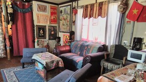 Un salon chaleureux avec un canapé, des fauteuils et une table basse. Les murs sont décorés de divers objets, notamment des tableaux encadrés et des drapeaux.