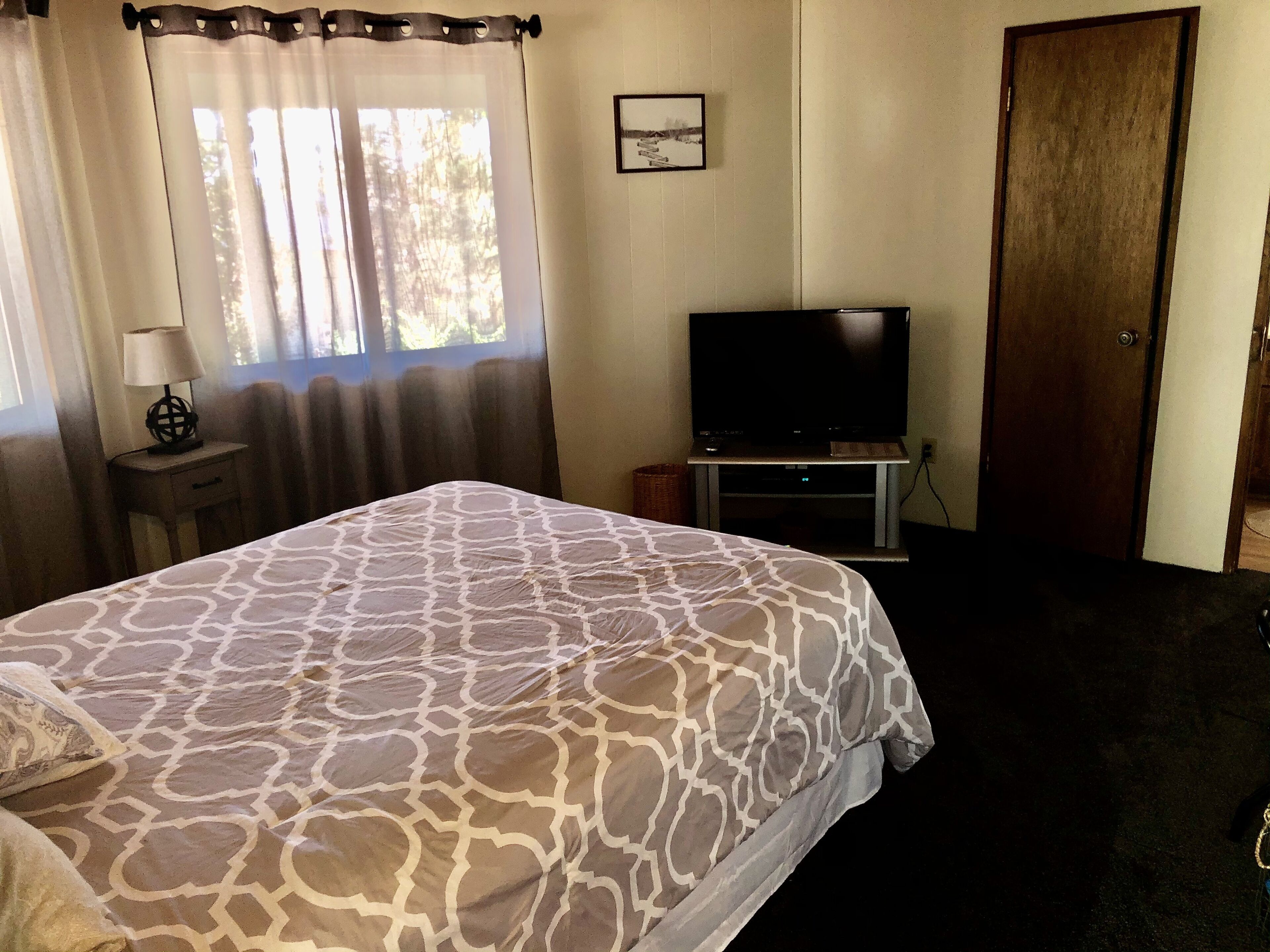 A hotel room with a bed, a television, a lamp, and a window with curtains.