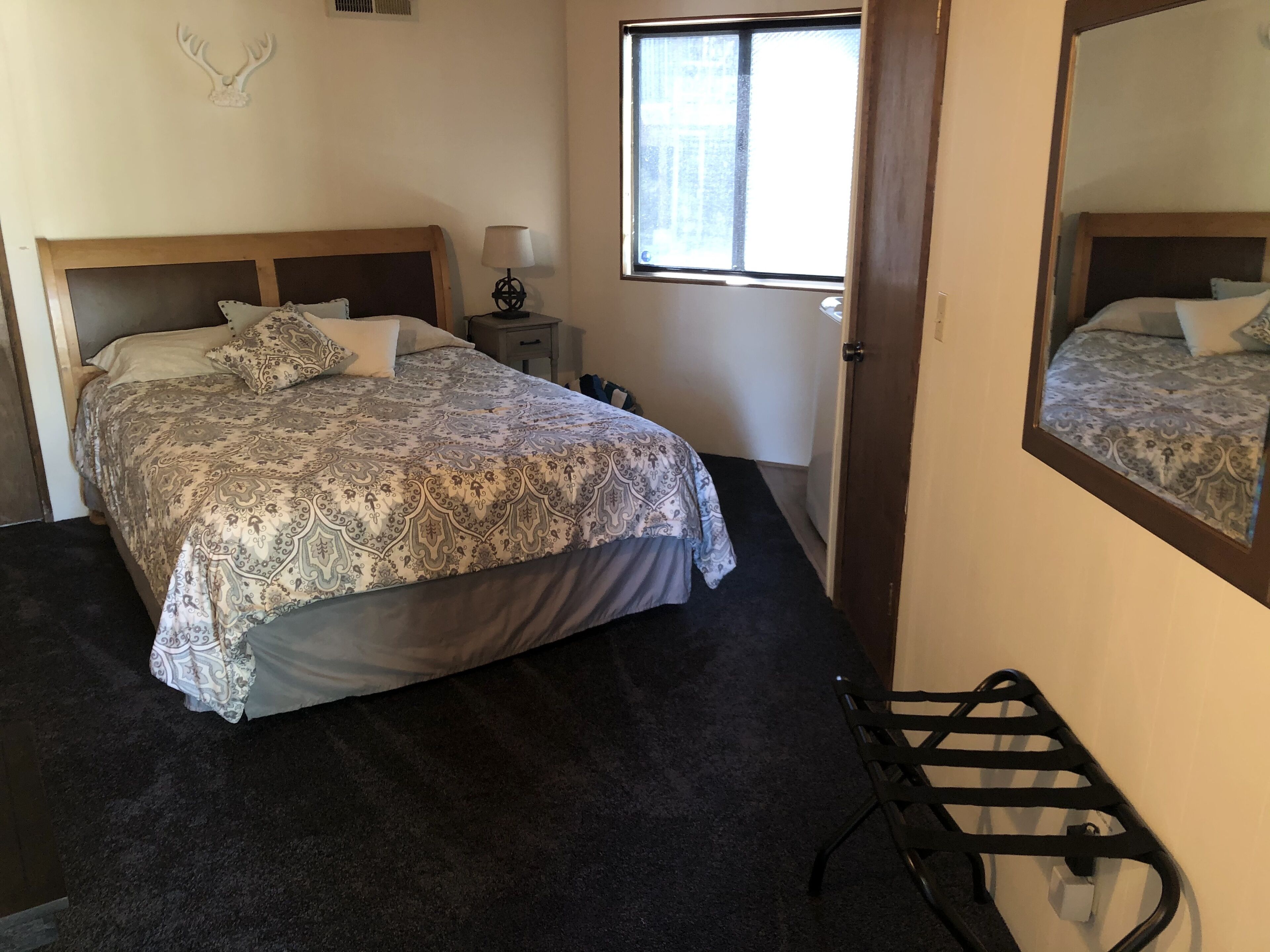 A bedroom with a bed, a nightstand, a lamp, a window, and a mirror.