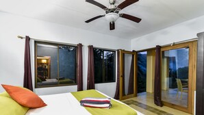 A hotel room with a bed, a ceiling fan, large windows with curtains, and a view of the outdoors. - Tropical villa nestled in the forest with a pool and waterfalls (Portalon)