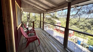 A wooden deck with red chairs and a table, overlooking a residential area with trees and houses.