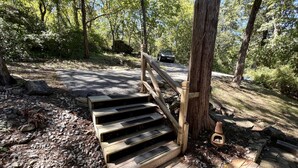 A wooden staircase leading up to a wooden deck surrounded by trees.