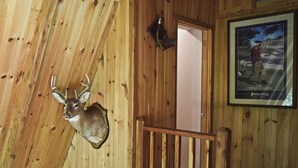 A wooden cabin interior with a mounted deer head on the wall, a framed picture of a golf course, and a wooden door. - Beautiful Mountain Top Private Log Cabin Lake And Mountain Views  Pet Friendly (Butler)
