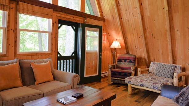 A cozy cabin interior with a wooden ceiling, a sofa, a patterned armchair, and a table with a book. - Beautiful Mountain Top Private Log Cabin Lake And Mountain Views  Pet Friendly (Butler)
