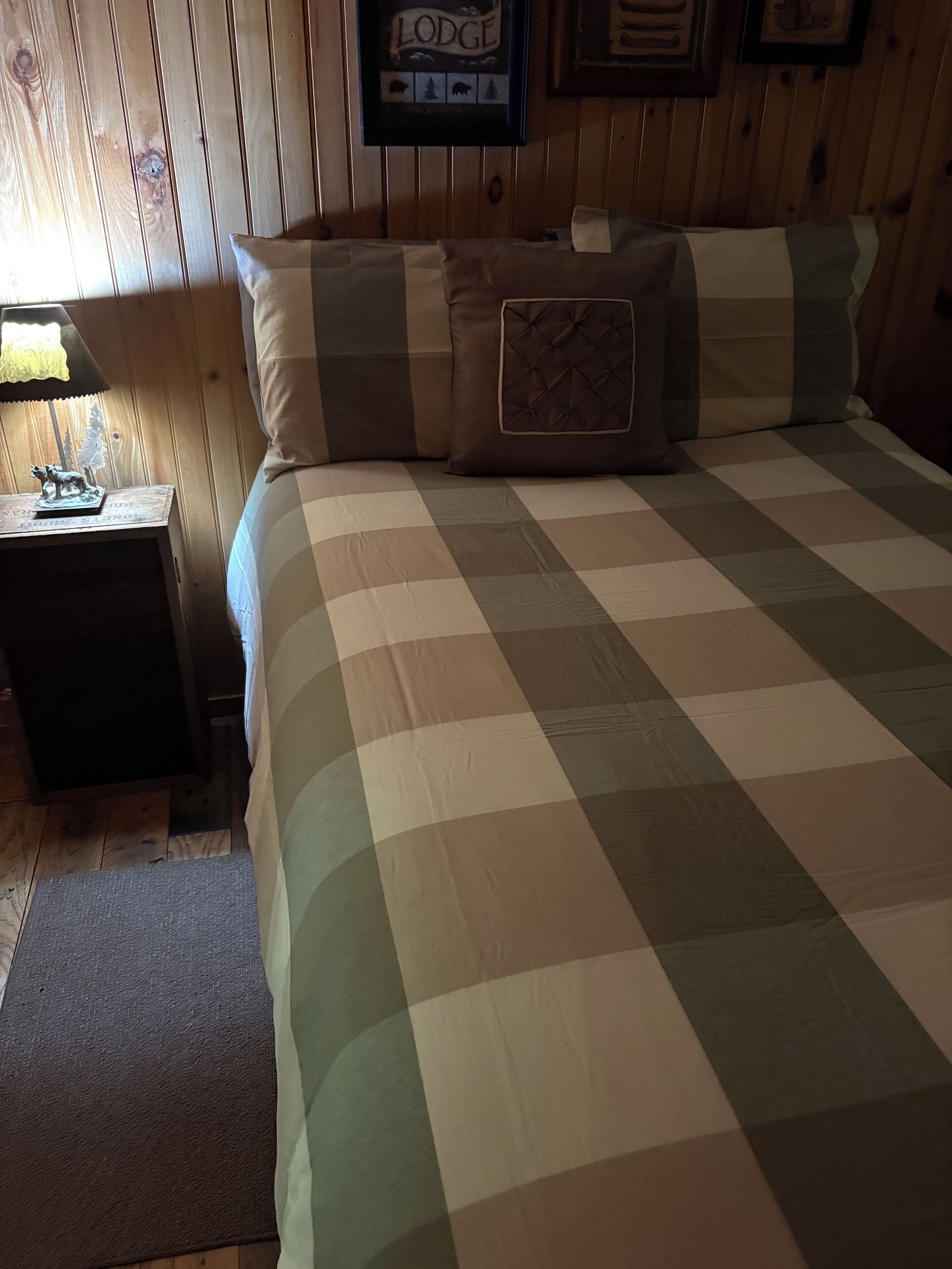 A cozy room with a checkered bedspread, a nightstand with a lamp, and a framed sign on the wall.