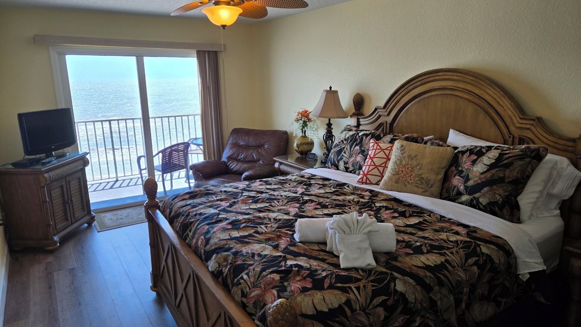 Habitación de hotel con una cama, televisión, sillón y vista al océano.