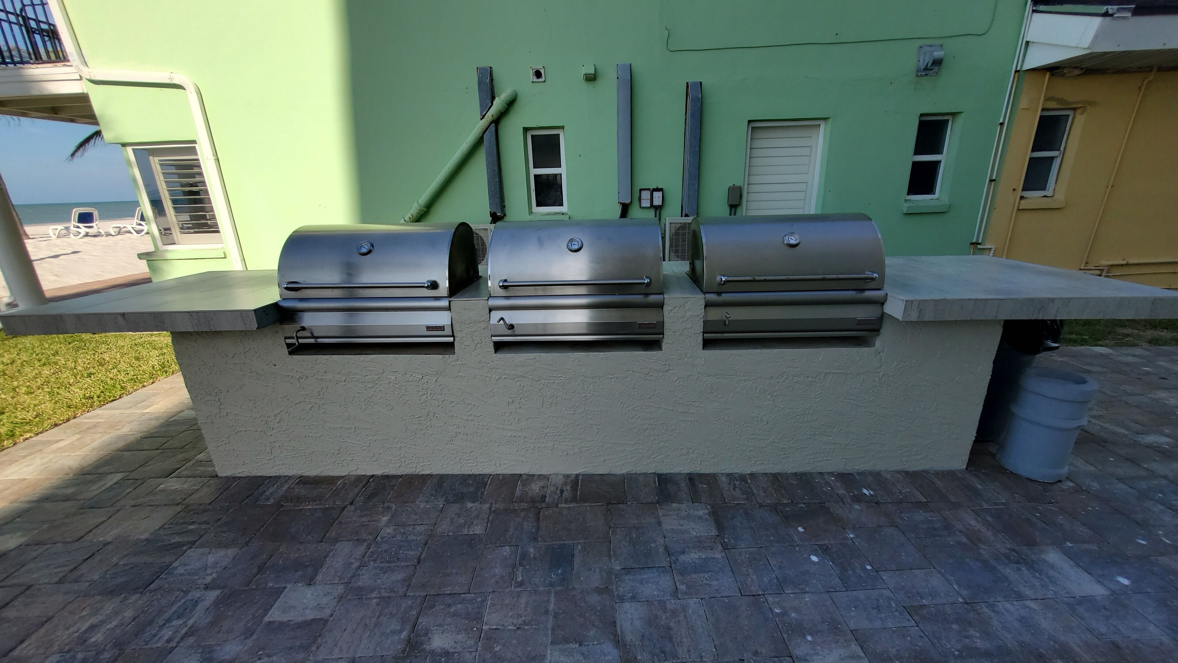 An outdoor grill station with three grills, a concrete countertop, and a view of the ocean.