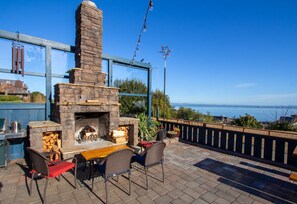 An outdoor patio with a stone fireplace, seating, and a view of the sea.