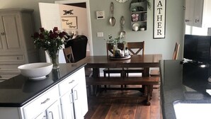 Una cocina con suelo de madera, armarios blancos, una mesa de comedor y un ventilador de techo.
