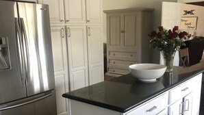 Una cocina moderna con armarios blancos, un refrigerador de acero inoxidable, una encimera negra y un bote de basura de acero inoxidable.