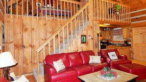 A wooden cabin interior with a red leather sofa, a wooden coffee table, and a staircase leading to an upper level. - MOUNTAIN HIDEAWAY - AUTHENTIC LOG CABIN MINUTES TO PARKWAY AND ATTRACTIONS!!! (Pigeon Forge)