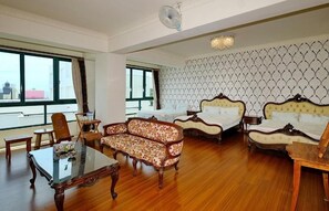 Une chambre d’hôtel dotée d’un grand lit, d’un canapé, d’une table à manger et offrant une vue sur la ville grâce à de grandes fenêtres.